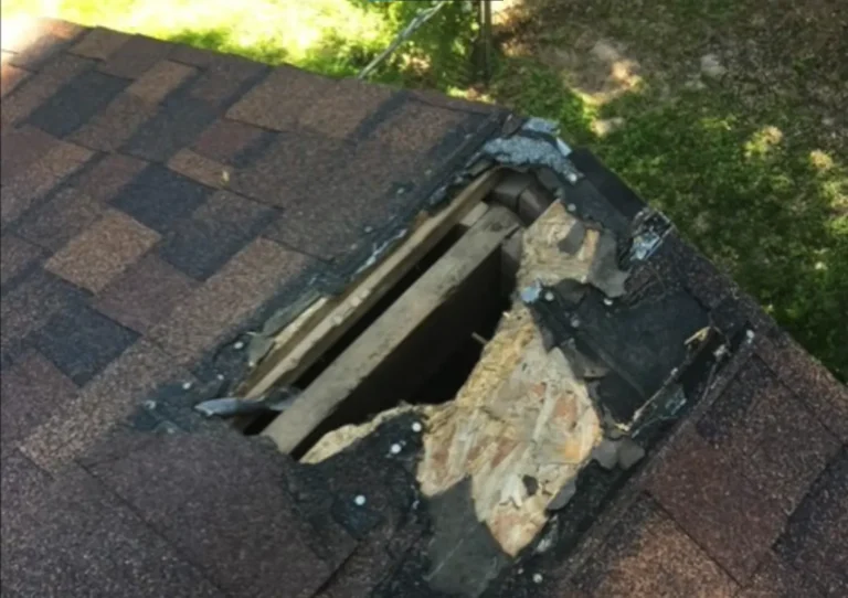 Hole in a shingled roof exposing timber rafters and roof sheathing