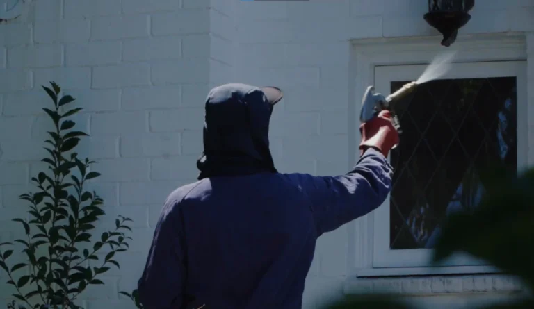 Technician in a hooded top spraying a treatment around a window on a white-painted brick wall