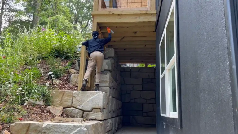 Pest control technician on stone steps spraying the underside of a timber deck